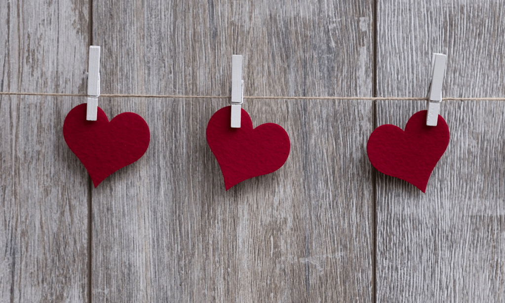Three red felt hearts hanging on a clothesline in front of a wooden wall