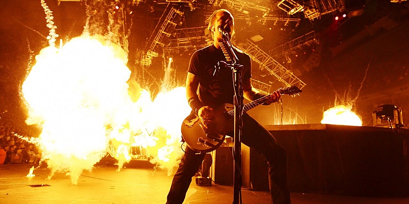 James Hetfield with Metallica in concert with flames behind him.