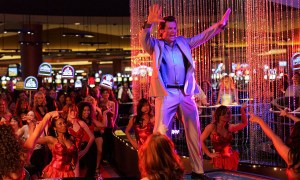 A man sings while standing on a table while the room full of women look on