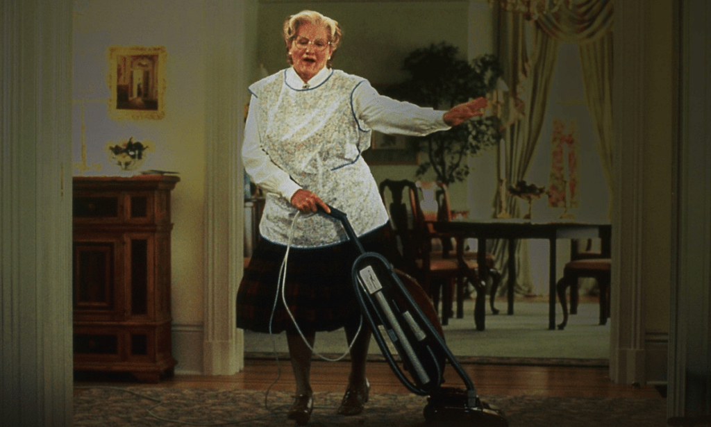 A man dressed as an old woman dancing with a vacuum cleaner