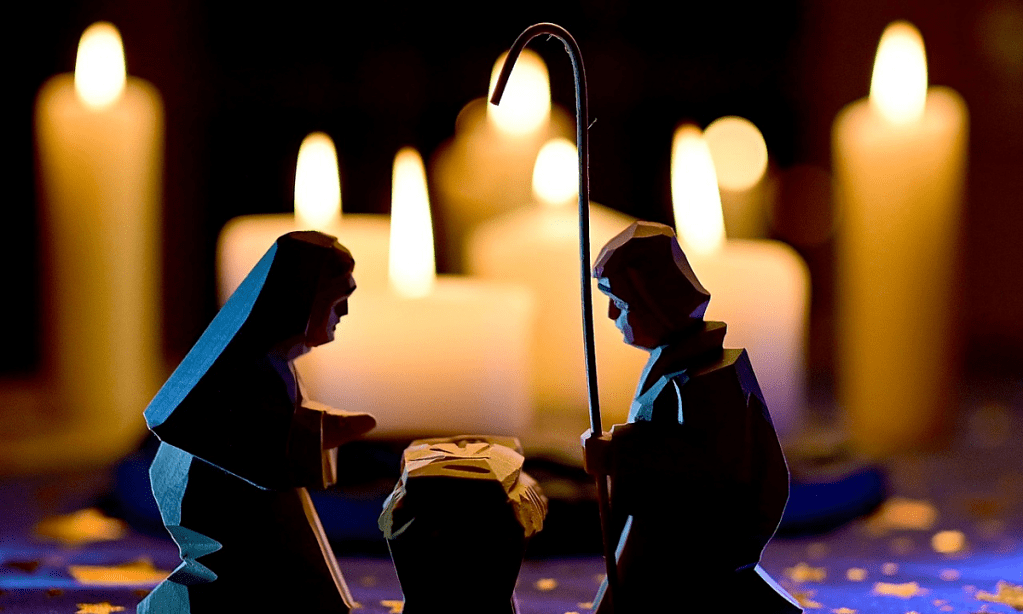 A simple nativity scene featuring wood carvings of Mary, Joseph and Jesus placed in front of candles.