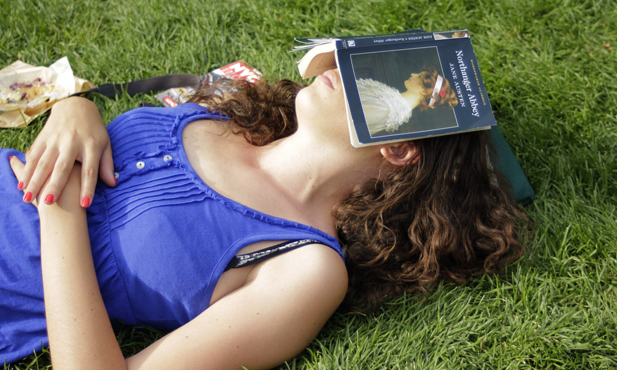 A woman asleep on the grass uses a Jane Austen book as a sun shield.