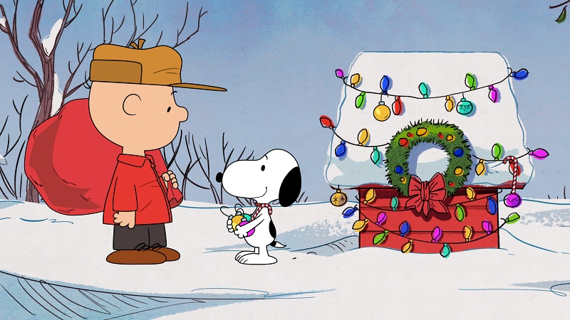 Charlie Brown and Snoopy in front of his decked out dog house.
