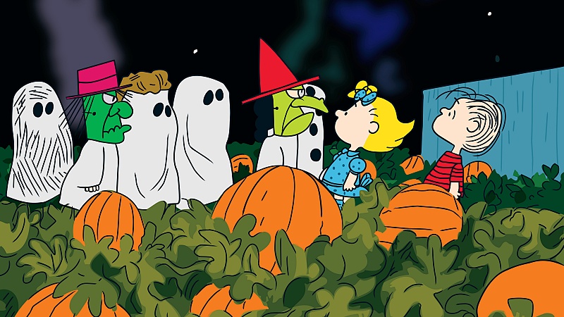 The Peanuts kids are in costume hanging out in a pumpkin patch.