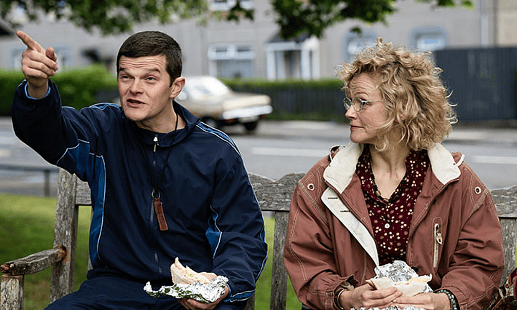 Robert Aramayo and Maxine Peake sit on a park bench eating lunch